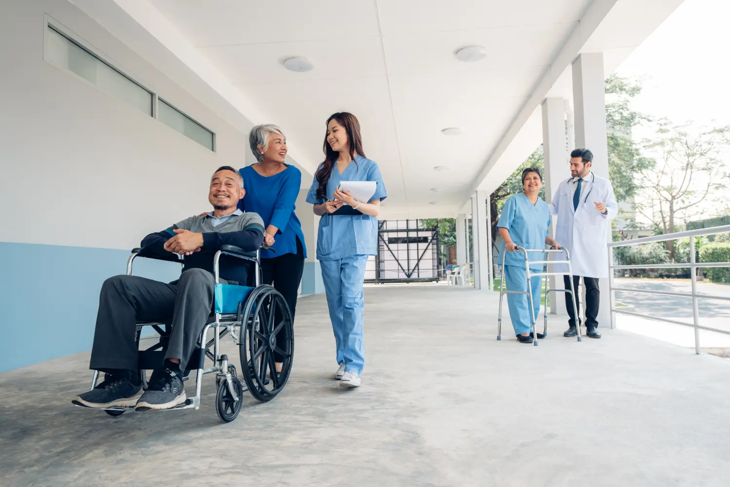 Arzt und Krankenschwester kümmern sich um eine reife Patientin, die im Krankenhaus im Rollstuhl sitzt, und unterhalten sich mit ihr.